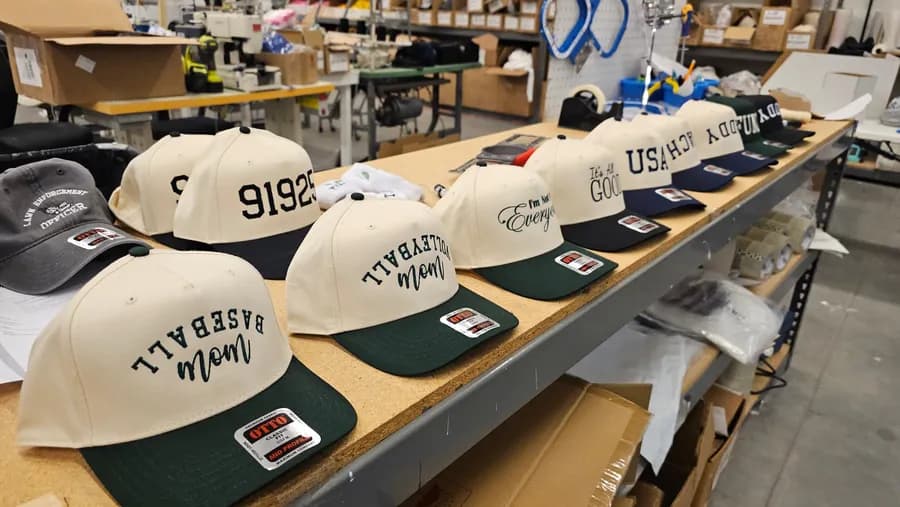 A row of finished embroidered caps on our work table, sewing machines and stock behind