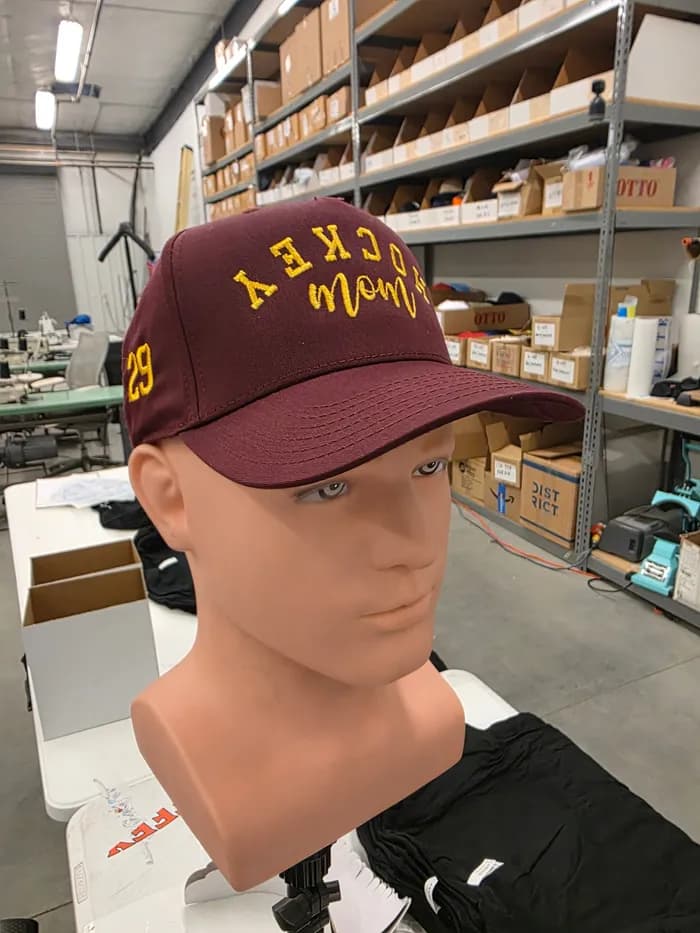 An embroidered cap on a mannequin in our shop, stock shelving behind