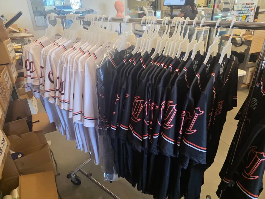 Finished jerseys on a rack in our shop, embroidery machines running in the background