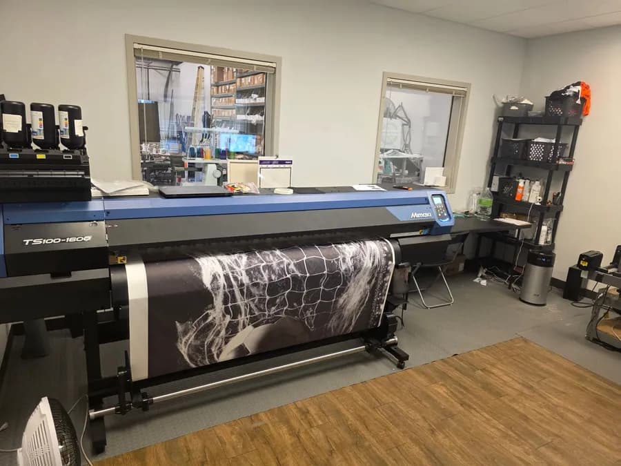 Our Mimaki dye-sublimation printer running a print, our shop visible through the windows behind it